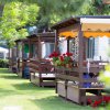 Villette con veranda in legno, ombreggiate e decorate con fiori rossi, su un prato verde.
