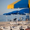 Spiaggia con lettini, ombrelloni blu e mare calmo sullo sfondo.