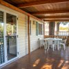 Veranda con tetto in legno, tavolo e sedie bianche, vista su giardino e alberi.