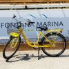 Una bicicletta gialla con cestino nero parcheggiata davanti a un cartello.
