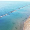 Spiaggia con ombrelloni e mare, frangiflutti visibili.