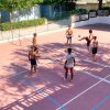 Persone giocano a footvolley su un campo con rete, circondato da alberi.