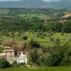 Casale di pietra circondato da alberi e prati collinari.