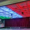 Soffitto colorato con luci a LED sopra un palco con tenda rossa.