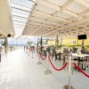 Ristorante all'aperto con sedie nere e corde rosse. Vista mare.