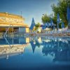 Piscina con lettini e ombrelloni blu accanto a un edificio.