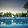 Piscina con lettini, ombrelloni blu e palme sullo sfondo.