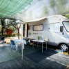 Camper parcheggiato con tavolo, sedie e tenda ombreggiante.