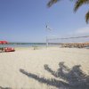 Spiaggia con rete da pallavolo, ombrelloni arancioni e bandiere, vicino al mare.