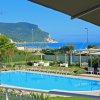 Piscina con sedie a sdraio, ombrelloni e vista sul mare e montagne.