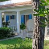 Una veranda con sedie bianche e finestre blu, circondata da alberi e giardino.