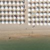 Spiaggia con file ordinate di ombrelloni bianchi.