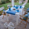 Tavolo da pranzo all'aperto con stoviglie blu e sedie in legno, su una terrazza con giardino.