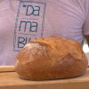 Persona con maglietta bianca e scritta, tenendo un pane casereccio su un tagliere.