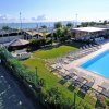 Vista di una piscina esterna con lettini e un campo da tennis vicino al mare.