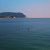 Mare calmo con persone che praticano surf, e una montagna sullo sfondo.