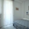Letto matrimoniale con copriletto blu e giallo, mensola con lampade blu, finestra con tende bianche.
