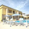 Edificio giallo a due piani con balconi, bordo piscina con ombrelloni blu.