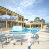 Piscina all'aperto con lettini e ombrelloni blu, edificio giallo sullo sfondo.
