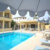 Piscina all'aperto con ombrelloni blu e un edificio giallo sullo sfondo.