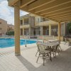 Area piscina con tavoli e sedie sotto una tettoia, edifici sullo sfondo.