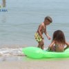 Due bambini giocano sulla spiaggia, uno seduto su un materassino verde in acqua.