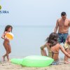 Famiglia in spiaggia, due adulti e due bambini giocano sulla sabbia vicino al mare.