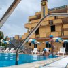 Piscina all'aperto con edificio giallo e ombrelloni blu. Bambino salta in piscina.