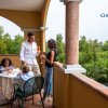 Famiglia su una terrazza, conversano mentre due bambini mangiano a un tavolo.