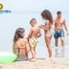 Famiglia al mare, con una donna seduta sulla sabbia e un uomo che cammina verso riva.