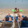 Spiaggia con persone su sdraio e bambini che giocano sulla sabbia.