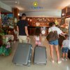 Famiglia con valigie al bancone della reception dell'hotel, vicino a un frigorifero con bevande.