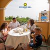 Famiglia seduta a tavola su una terrazza, con bevande e cibo.