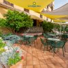 Terrazza esterna con tavolini e sedie verdi, piante e fiori colorati sotto vele ombreggianti.