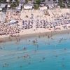 Spiaggia affollata con lettini, ombrelloni e bagnanti nel mare.