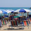 Spiaggia con lettini colorati e ombrelloni blu, mare sullo sfondo.