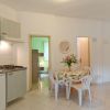 Cucina e zona pranzo con tavolo rotondo, sedie di plastica, fiori e toni chiari.
