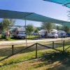 Camper parcheggiati sotto teloni ombreggianti in un campeggio.