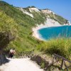 Sentiero verso una spiaggia con mare blu e scogliere.