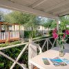 Una veranda con tavolo bianco e fiori, circondata da siepi e bungalow.