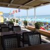 Terrazza con tavoli e sedie, vista su spiaggia con ombrelloni azzurri e mare.