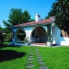 Casa con portico e tavolo da esterno, circondata da prato e alberi.