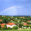 Paesaggio collinare con case dai tetti rossi, arcobaleno nel cielo.