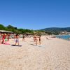 Una spiaggia di ciottoli con persone che prendono il sole e fanno ginnastica, montagne sullo sfondo.