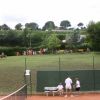 Campo da tennis con due persone, collina sullo sfondo con spettatori e cavalli.