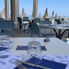 Tavoli apparecchiati in un ristorante all'aperto con vista mare e sedie blu.