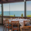Sala da pranzo con tavoli apparecchiati, sedie in legno e grandi finestre con vista mare.