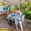 Due persone sedute a un tavolo su una veranda in legno, circondate da vegetazione.