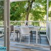 Porta aperta su una veranda con tavolo apparecchiato e ringhiera bianca immersa nel verde.