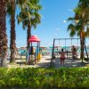 Area giochi con altalene e scivoli tra palme vicino alla spiaggia.